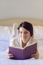 Caucasian woman laying on bed reading book