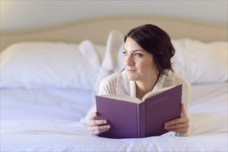 Pensive Caucasian woman laying on bed reading book