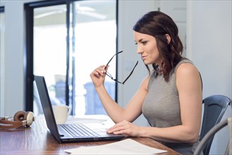 Pensive Caucasian woman holding eyeglasses using laptop