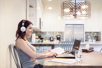 Caucasian woman listening to headphones reading paperwork using laptop