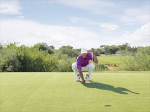 Hispanic golfer crouching on golf course