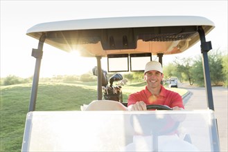 Portrait of Hispanic golfer driving golf cart