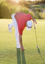 Hispanic golfer reaching into hole on golf course