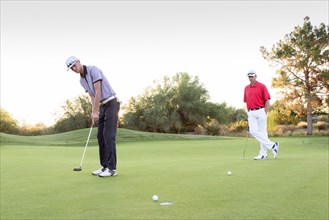 Man watching friend putting on golf course