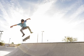 Hispanic man performing mid-air trick on skateboard