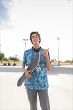 Portrait of smiling Hispanic man holding skateboard