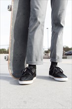Legs of Hispanic man holding skateboard