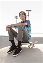Portrait of smiling Hispanic man sitting on skateboard
