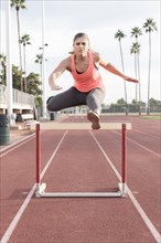 Hispanic woman jumping over hurdle