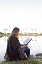 Hispanic woman sitting bear lake reading book