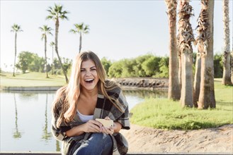 Laughing Hispanic woman holding cell phone near pond