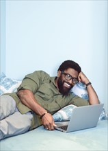 Smiling black man laying on bed using laptop
