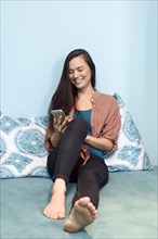 Smiling mixed race woman sitting on bed texting on cell phone