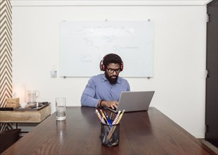 Black businessman wearing headphones using laptop