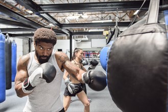 Man and women wearing boxing gloves hitting heavy bags