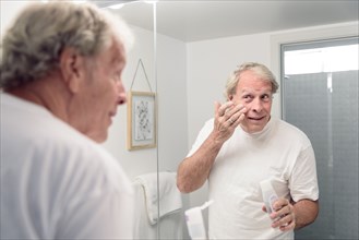 Caucasian man applying lotion to face in mirror