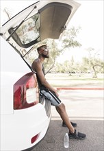 Black man sitting on car hatchback