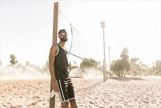 Black man leaning on beach volleyball net