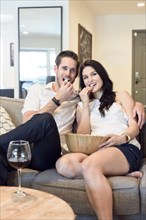 Smiling Caucasian couple sitting on sofa watching television