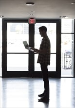 Caucasian man standing near doorway using laptop