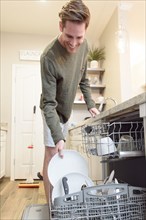 Smiling Caucasian man loading dishwasher