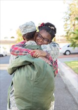 Black woman soldier hugging daughter in street