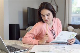 Caucasian woman reading paperwork near laptop