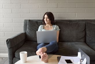 Caucasian woman sitting on sofa using laptop