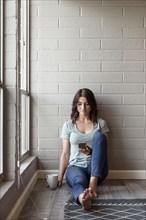 Caucasian woman sitting on floor texting on cell phone