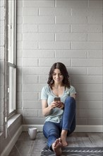 Caucasian woman sitting on floor texting on cell phone