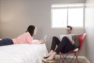 Caucasian couple using digital tablet and laptop in bedroom