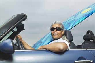 Senior man driving a convertible with a surfboard in it