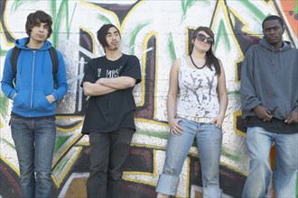 Group of young adults leaning against graffitied wall