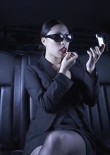 Asian businesswoman applying make up in back seat of car