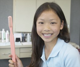 Asian girl holding large toothbrush at dentist's office