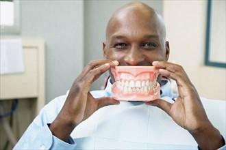 African man in dentist's chair holding up model of teeth