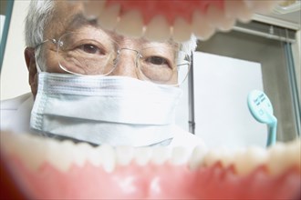 Shot from mouth looking out at senior Asian male dentist