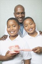 African male dentist with twin boys holding toothbrush and model of teeth