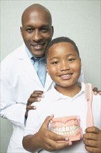 African male dentist with boys holding toothbrush and model of teeth