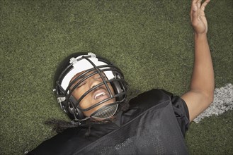 Young African man in football uniform laying on field