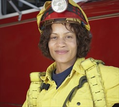 African female firefighter leaning against fire truck