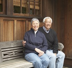Senior Asian couple smiling and sitting on bench outdoors