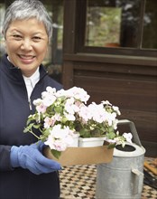 Senior Asian woman holding potted plants outdoors