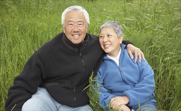 Senior Asian couple sitting in tall grass smiling