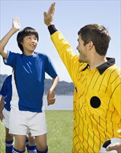 Asian boy high-fiving soccer coach