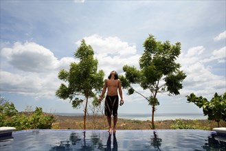 Asian man standing on edge of infinity swimming pool