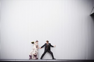 Playful bride and groom standing near wall