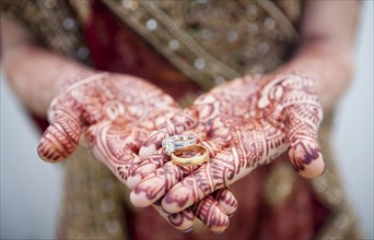 Caucasian woman with Indian henna tattoos on her hands holding wedding rings