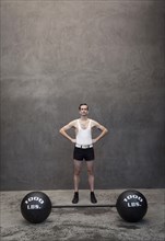 Skinny Caucasian weight lifter standing by weights
