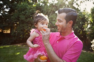 Father feeding daughter orange outdoors